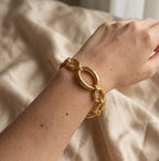 Gros plan réaliste sur le bracelet doré Victoire Vibrante, composé de maillons ovales et ronds polis, porté au poignet d'un mannequin. Le fond est un tissu beige froissé.
