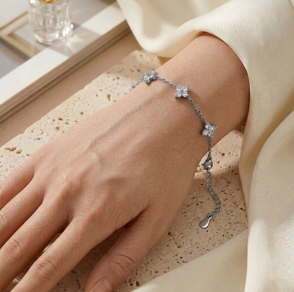 Gros plan réaliste du bracelet argenté Margaux Fine porté au poignet d'une femme. On distingue le grain de peau naturel et les cinq trèfles délicats sertis de cristaux étincelants qui épousent la courbe du bras sur une fine chaîne maille forçat dorée.