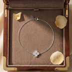 Vue de dessus du bracelet argenté Sia - Cristalline présenté dans un coffret de luxe en bois. Le bijou entoure délicatement trois pétales de rose séchés sur un fond en suédine beige.