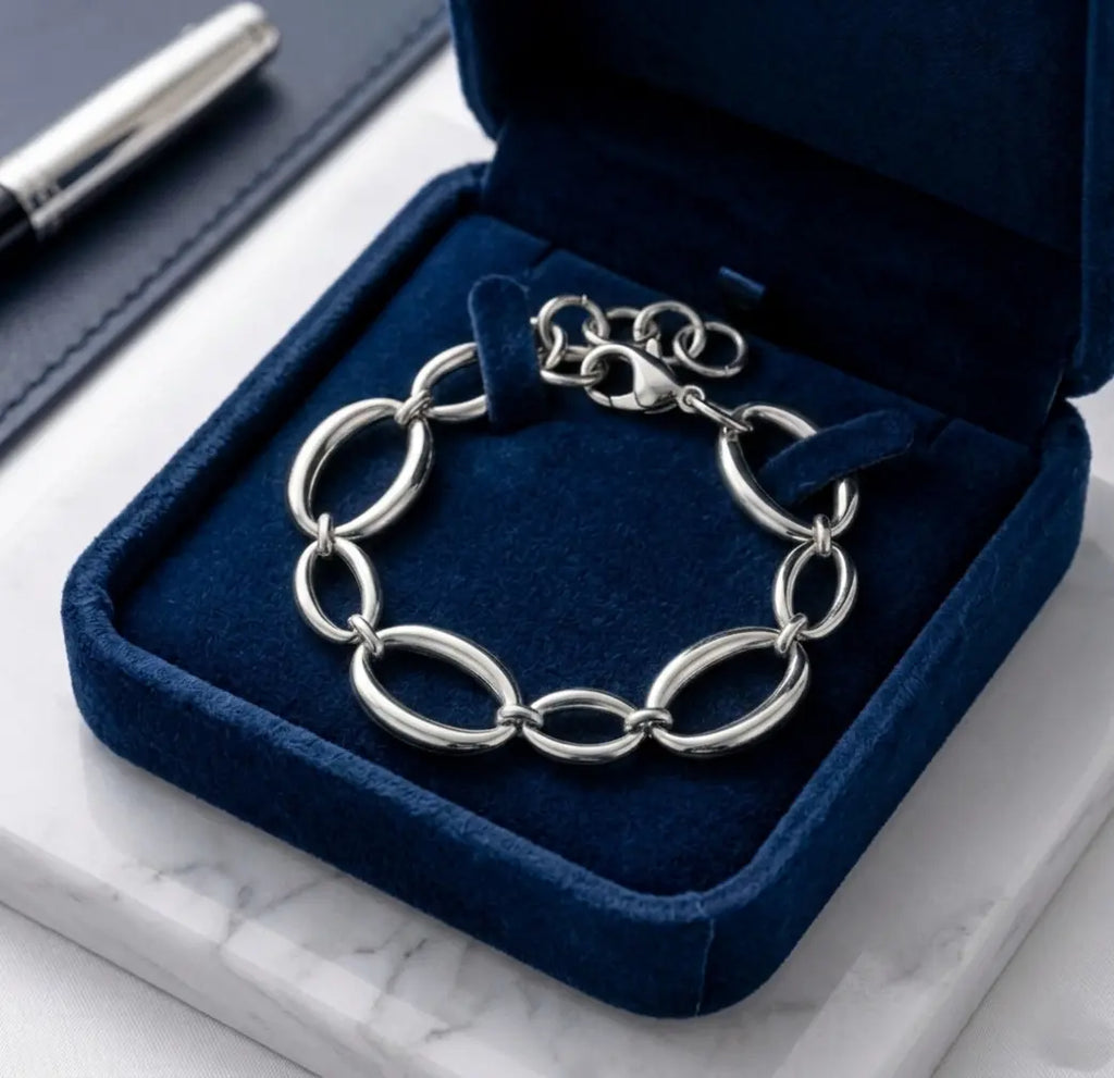 Mise en scène luxueuse du bracelet argenté Victoire Vibrante, présenté dans un écrin de velours bleu nuit ouvert. L'écrin repose sur du marbre blanc. Un stylo plume argenté est visible en arrière-plan.