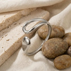 Bracelet Lyra argenté disposé dans un décor minéral, soulignant sa forme de goutte étirée et sa résistance au quotidien.