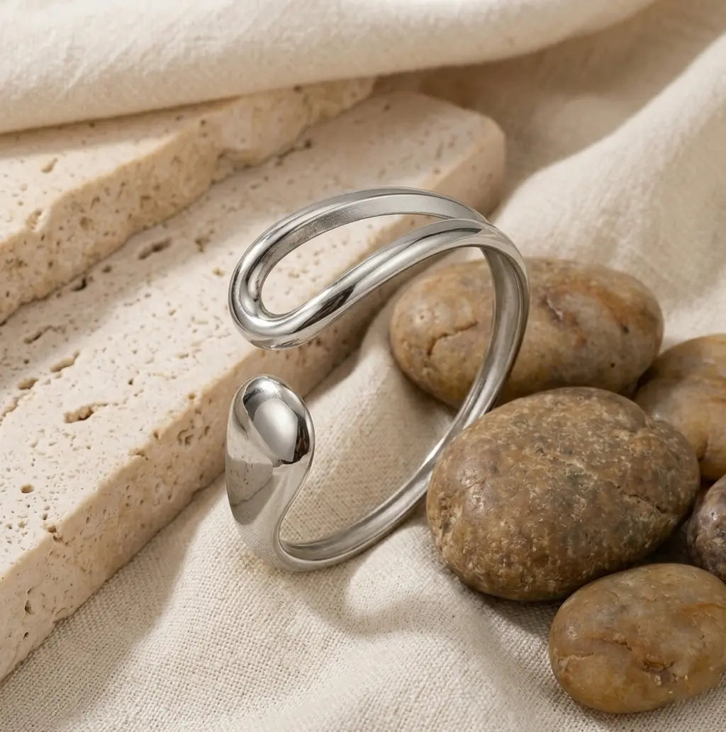 Bracelet Lyra argenté disposé dans un décor minéral, soulignant sa forme de goutte étirée et sa résistance au quotidien.