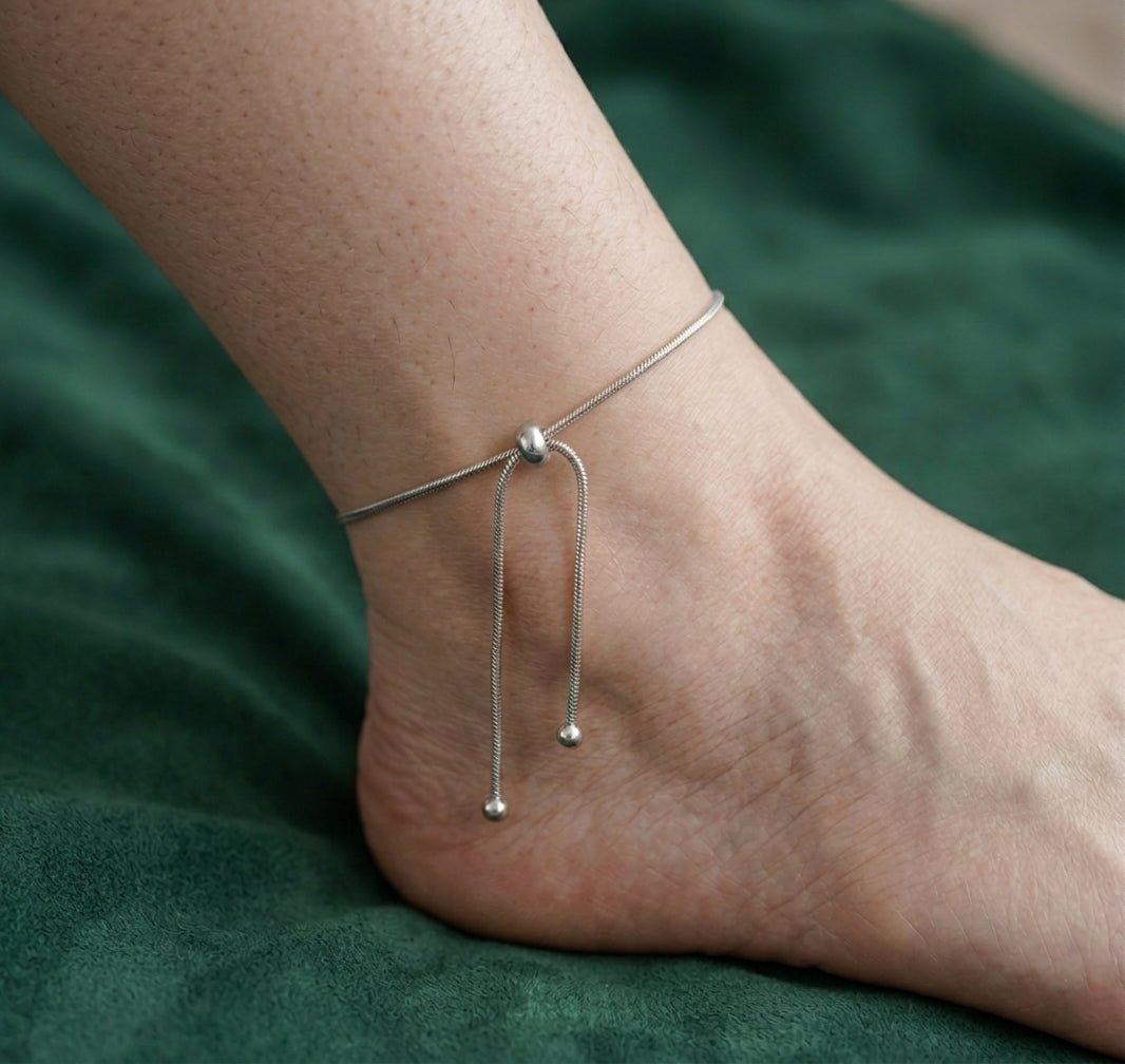 Gros plan sur la cheville d'une femme portant le bracelet Sienne Infinie argenté, montrant la maille serpent et le fermoir coulissant ajustable.