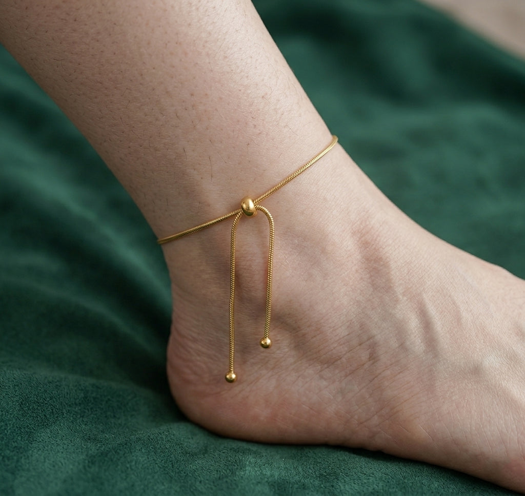 Gros plan sur la cheville d'une femme portant le bracelet Sienne Infinie doré, montrant la maille serpent et le fermoir coulissant ajustable.