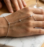 Gros plan macro du bracelet de main Lola Libre en argent sterling 925, sur marbre de Carrare. Des gouttes d'eau sont délicatement posées sur la chaîne fleurie et scintillante, évoquant la pureté et l'éclat naturel. Le bijou semble flotter sur la main.