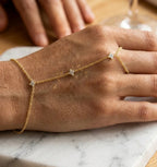 Très gros plan macro du bracelet de main Lola Libre en plaqué or, reposant sur une surface de marbre de Carrare blanc. La chaîne fine et les motifs floraux sertis de cristaux sont nets et détaillés, soulignant la finesse de l'artisanat.