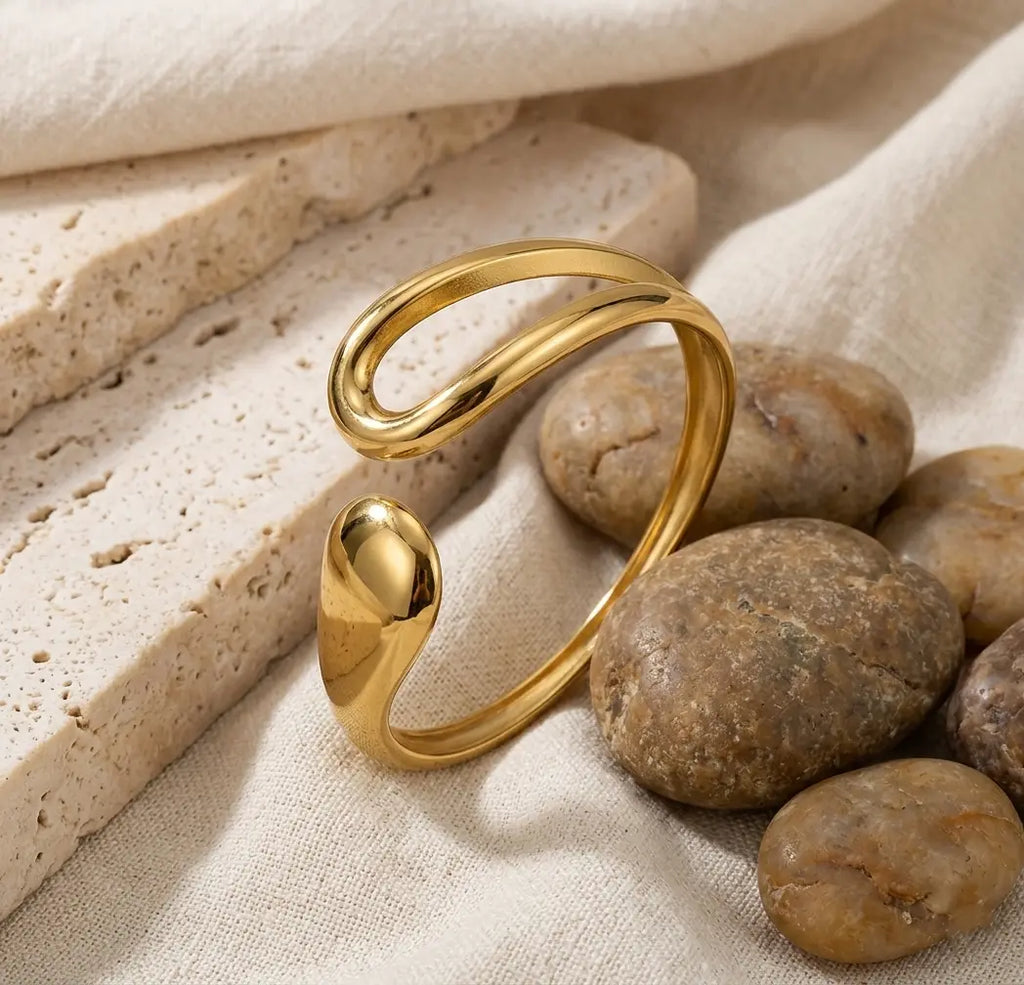Bracelet Lyra doré disposé dans un décor minéral, soulignant sa forme de goutte étirée et sa résistance au quotidien.