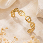 Bracelet jonc Clara doré à maillons style maille marine, présenté sur un support minéral beige avec des fleurs séchées.
