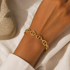 Poignet féminin portant le bracelet jonc Clara doré à maillons marins, sur un fond de tissu blanc texturé.