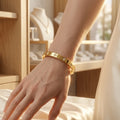 Gros plan du bracelet jonc doré Alix Distinguée avec motifs trèfles sertis de cristaux, porté au poignet d'une femme dans une boutique de luxe.