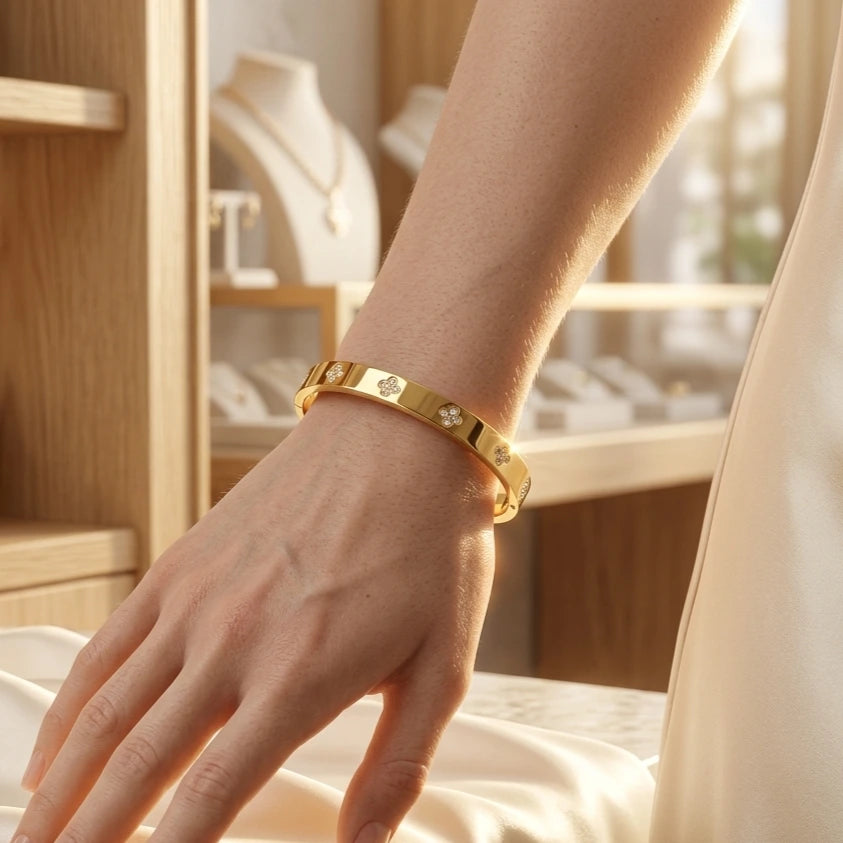 Gros plan du bracelet jonc doré Alix Distinguée avec motifs trèfles sertis de cristaux, porté au poignet d'une femme dans une boutique de luxe.
