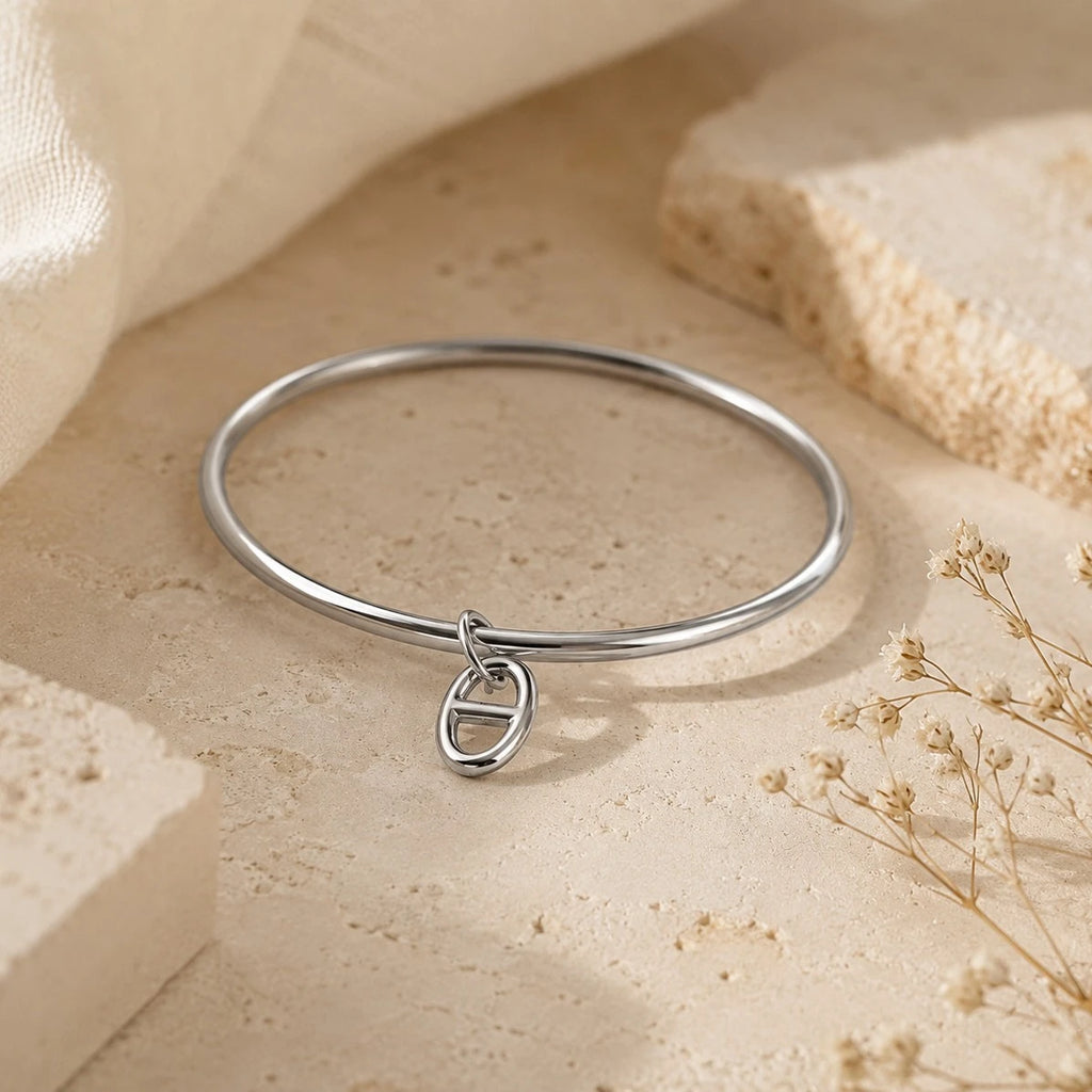Bracelet jonc Stella en argent avec un pendentif maille marine, posé sur un support en pierre beige entouré de fleurs séchées.