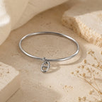 Bracelet jonc Stella en argent avec un pendentif maille marine, posé sur un support en pierre beige entouré de fleurs séchées.