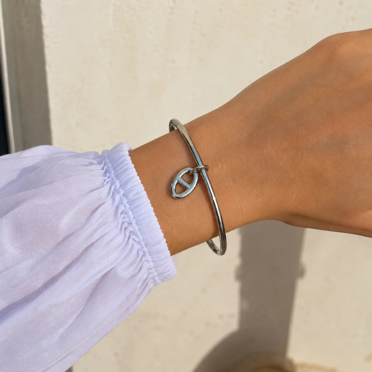 Poignet féminin portant le bracelet jonc Stella en argent à maille marine, associé à un haut blanc à manches bouffantes.
