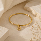 Bracelet jonc Stella doré avec pendentif maille marine, posé sur une pierre travertin beige entourée de fleurs séchées.