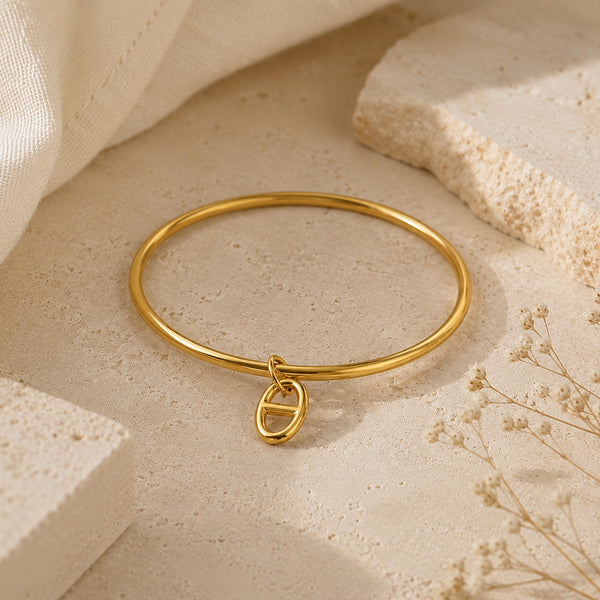 Bracelet jonc Stella doré avec pendentif maille marine, posé sur une pierre travertin beige entourée de fleurs séchées.