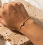 Main portant le bracelet en acier inoxydable Isaline Scintillante avec son solitaire, posée sur une pierre de marbre brut.