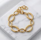 Photographie à plat (flat lay) du bracelet doré Victoire Vibrante. Il est posé sur un bloc de marbre blanc veiné, sur un fond de satin blanc. Les maillons ovales et le fermoir mousqueton sont bien visibles.