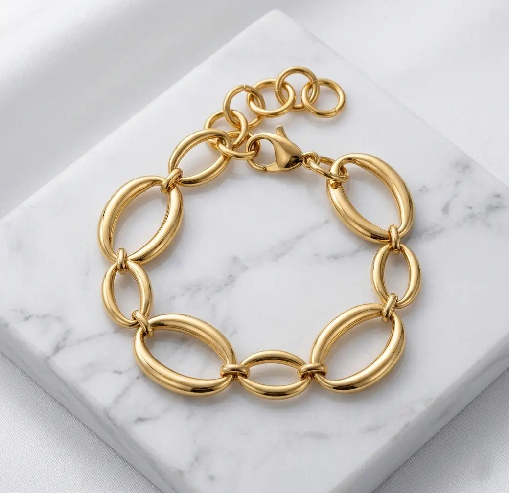 Photographie à plat (flat lay) du bracelet doré Victoire Vibrante. Il est posé sur un bloc de marbre blanc veiné, sur un fond de satin blanc. Les maillons ovales et le fermoir mousqueton sont bien visibles.