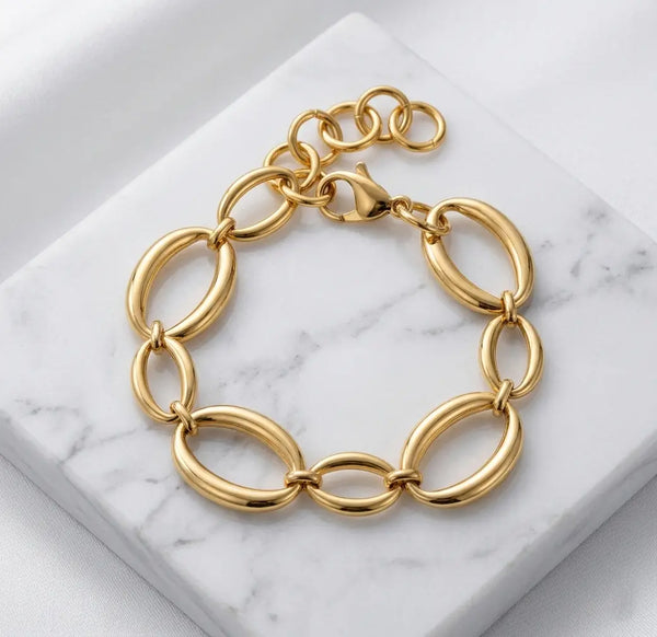Photographie à plat (flat lay) du bracelet doré Victoire Vibrante. Il est posé sur un bloc de marbre blanc veiné, sur un fond de satin blanc. Les maillons ovales et le fermoir mousqueton sont bien visibles.