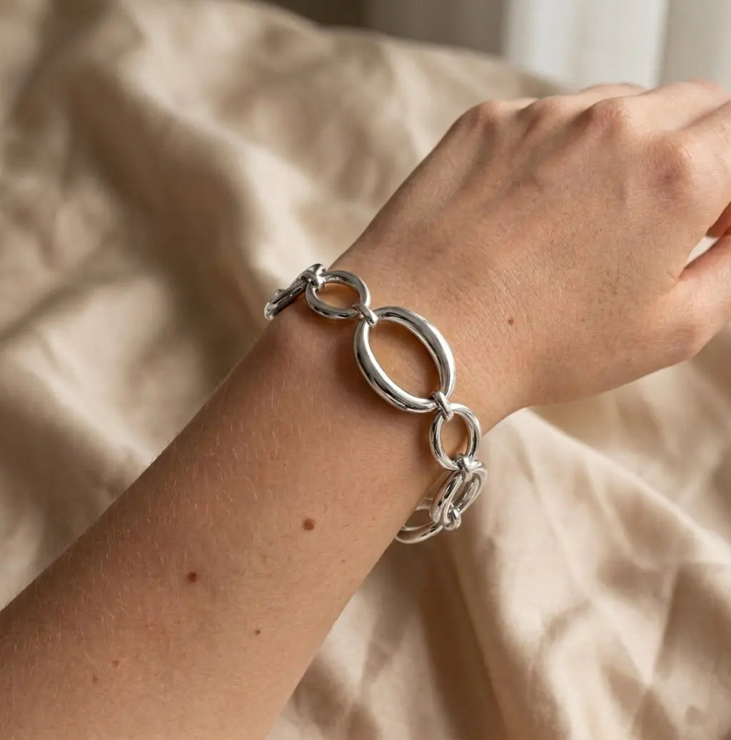 Gros plan réaliste sur le bracelet argenté Victoire Vibrante, composé de maillons ovales et ronds polis, porté au poignet d'un mannequin. Le fond est un tissu beige froissé.