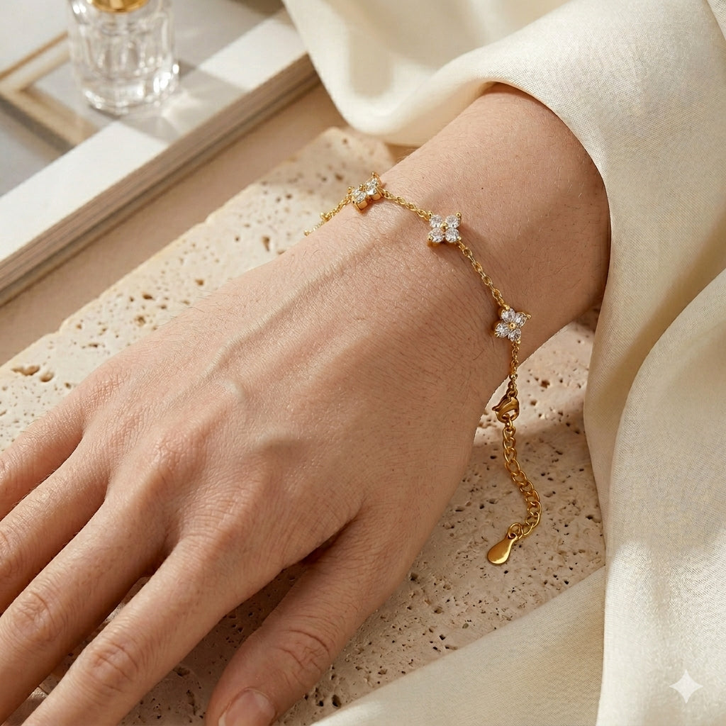 Gros plan réaliste du bracelet en acier inoxydable doré Margaux Fine porté au poignet d'une femme. On distingue le grain de peau naturel et les cinq trèfles délicats sertis de cristaux étincelants qui épousent la courbe du bras sur une fine chaîne maille forçat dorée.