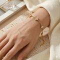 Gros plan réaliste du bracelet en acier inoxydable doré Margaux Fine porté au poignet d'une femme. On distingue le grain de peau naturel et les cinq trèfles délicats sertis de cristaux étincelants qui épousent la courbe du bras sur une fine chaîne maille forçat dorée.