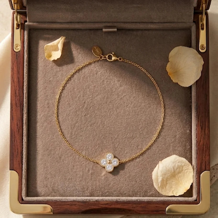 Vue de dessus du bracelet doré Sia - Cristalline présenté dans un coffret de luxe en bois. Le bijou entoure délicatement trois pétales de rose séchés sur un fond en suédine beige.