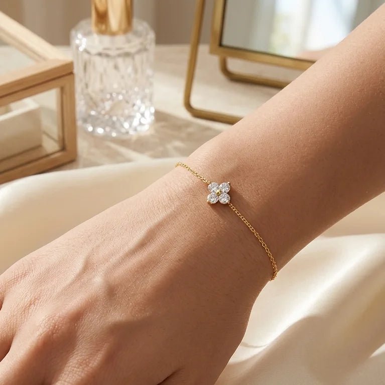 Bracelet Sia - Cristalline en finition or porté au poignet. La fine chaîne dorée et le trèfle scintillant contrastent élégamment sur la peau, avec un arrière-plan flou suggérant un intérieur raffiné.