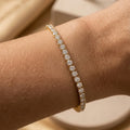 Gros plan du bracelet tennis Théa Absolue en finition dorée avec strass scintillants sur peau hâlée.
