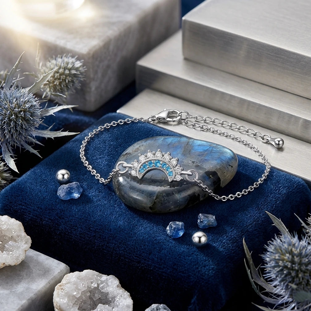 Le bracelet argenté Séléné avec son pendentif lune orné de pierres bleues, posé sur une pierre polie de labradorite et un présentoir en velours bleu marine.