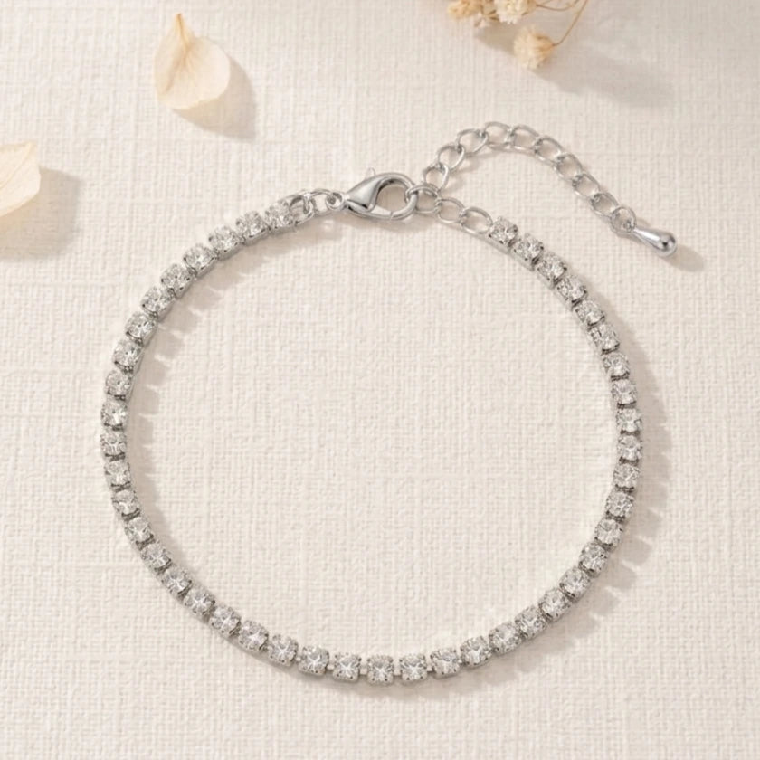 Bracelet fin argenté Théa Absolue posé à plat sur fond clair texturé avec fleurs séchées.