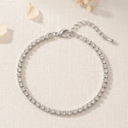 Bracelet fin argenté Théa Absolue posé à plat sur fond clair texturé avec fleurs séchées.