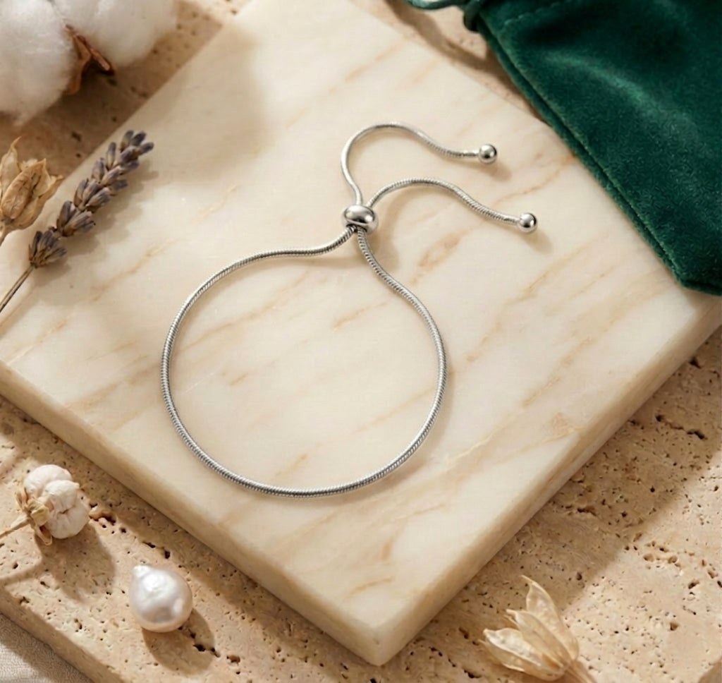 Composition élégante du bracelet de cheville Sienne Infinie argent sur un bloc de marbre, entouré de lavande et d'un pochon vert émeraude.