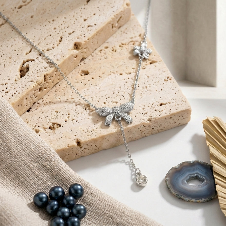 Présentation à plat (flatlay) du collier Adeline la Charmante argenté fin sur un bloc de pierre, entouré de perles bleues et d'une agate.