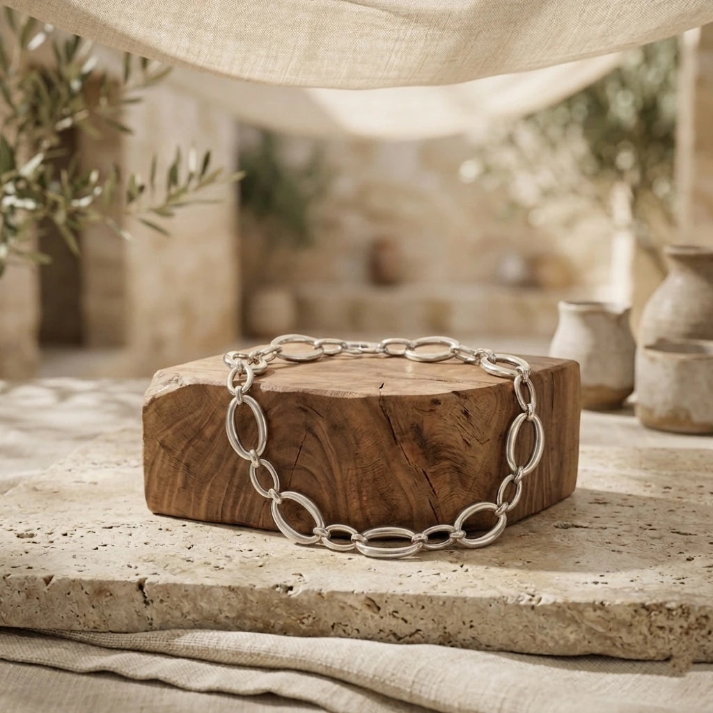 Collier Nina Désirable en argent posé sur un bloc de bois brut et une dalle de pierre calcaire, dans un décor méditerranéen ensoleillé avec oliviers.