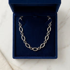 Vue de dessus du collier Nina Désirable en argent présenté dans son écrin ouvert en velours bleu roi, posé sur une surface de marbre blanc.