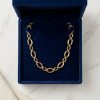 Vue de dessus du collier Nina Désirable en or présenté dans son écrin ouvert en velours bleu roi, posé sur une surface de marbre blanc.