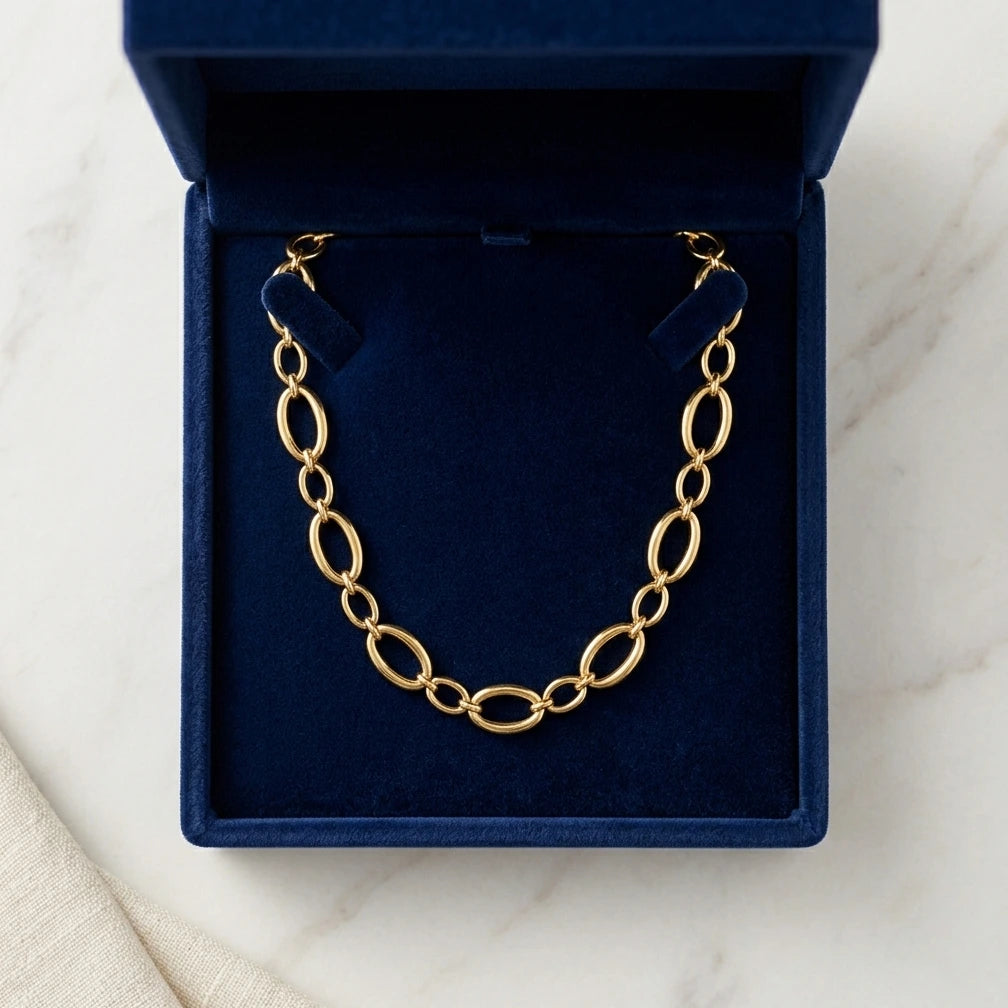 Vue de dessus du collier Nina Désirable en or présenté dans son écrin ouvert en velours bleu roi, posé sur une surface de marbre blanc.
