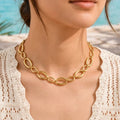 Gros plan sur une femme portant le collier Nina Désirable en or, assorti à un top en crochet blanc, sur une terrasse ensoleillée face à la mer.