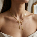 Gros plan du collier nœud Izia Enlacé en finition dorée, porté au cou d'une mannequin vêtue d'un haut blanc satiné.