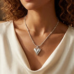 Close-up d'une mannequin portant le collier Yuna Romantique en argent. Le pendentif en forme de cœur bombé et poli reflète la lumière, suspendu à une fine chaîne perlée dorée sur un haut drapé blanc élégant.