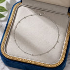 Image du collier Yzée argenté soigneusement présenté dans un écrin de luxe ouvert. Le bijou en acier argenté est disposé en boucle sur le fond en velours gris perle de la boîte, encadré par le bord en velours bleu roi et la frise dorée de l'écrin. Une présentation parfaite pour un cadeau précieux et intemporel.