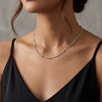 Gros plan du collier Yzée argenté porté par une mannequin au décolleté élégant. La fine chaîne à perles repose délicatement sur la peau, juste au-dessus du bord d'un top en soie noire. L'image capture la longueur parfaite du collier et sa subtilité, idéale pour un look quotidien ou chic.