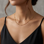 Gros plan du collier Yzée doré porté par une mannequin au décolleté élégant. La fine chaîne à perles repose délicatement sur la peau, juste au-dessus du bord d'un top en soie noire. L'image capture la longueur parfaite du collier et sa subtilité, idéale pour un look quotidien ou chic.