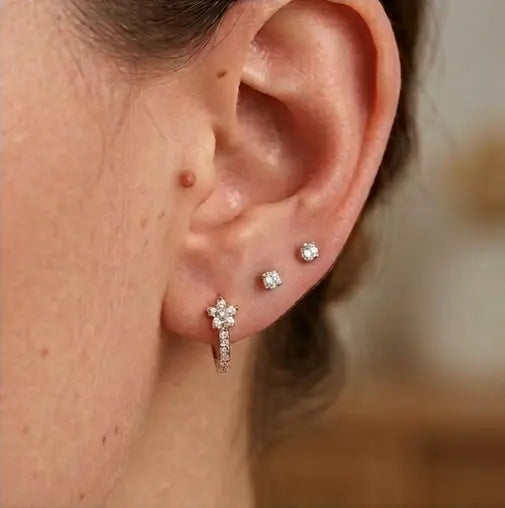 Le porté d'une mini-créole huggie Iris en acier inoxydable argenté et zircons au lobe, associée à deux clous d'oreilles en diamant pour un look chic.