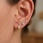 Le porté d'une mini-créole huggie Iris en acier inoxydable doré et zircons au lobe, associée à deux clous d'oreilles en diamant pour un look chic.