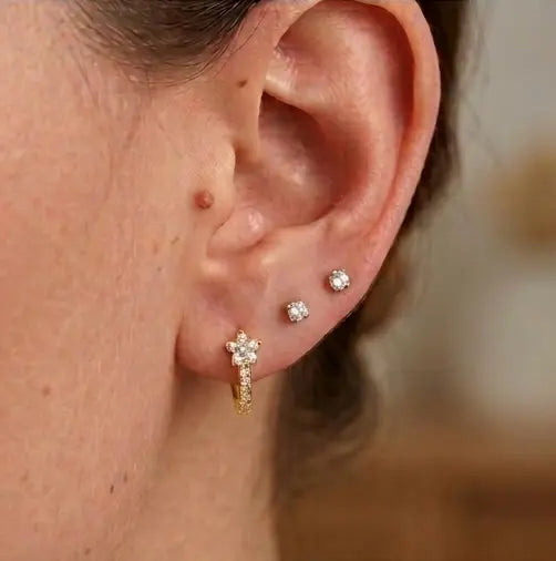 Le porté d'une mini-créole huggie Iris en acier inoxydable doré et zircons au lobe, associée à deux clous d'oreilles en diamant pour un look chic.