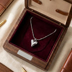Collier Yuna Romantique argenté présenté dans un luxueux écrin en bois foncé avec un intérieur en velours bordeaux. La chaîne est élégamment disposée pour montrer le pendentif cœur poli.