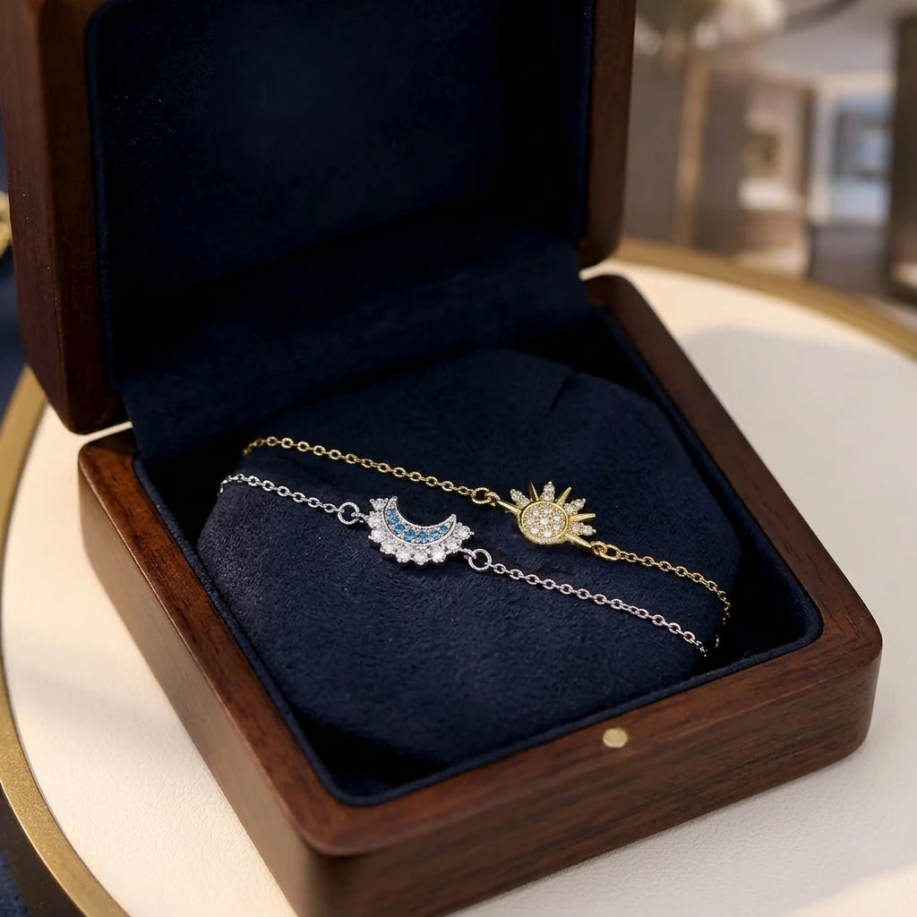 Un écrin en bois ouvert avec un intérieur en velours bleu marine, présentant le duo de bracelets Hélios et Séléné (un soleil doré et une lune argentée) posés côte à côte.